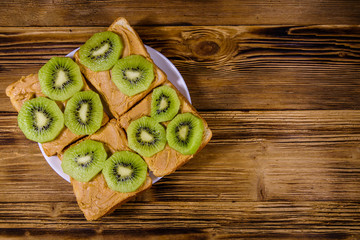 Sandwiches with peanut butter and sliced kiwi fruits in plate on a wooden table. Top view