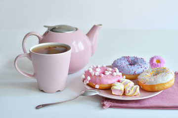 pink teapot, cup of tea and colorful delicious doughnuts