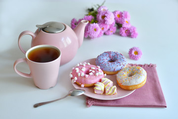 pink teapot, cup of tea and colorful delicious doughnuts