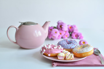 pink teapot, cup of tea and colorful delicious doughnuts