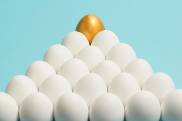 Concept of individuality, exclusivity, better choice. One golden egg among white eggs on blue background.