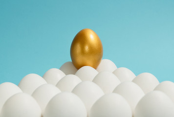 Concept of individuality, exclusivity, better choice. One golden egg among white eggs on blue...