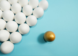 Concept of individuality, exclusivity, better choice. One golden egg among white eggs on blue background.