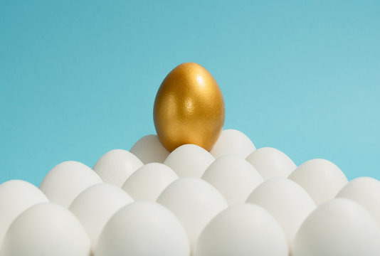Concept of individuality, exclusivity, better choice. One golden egg among white eggs on blue background.