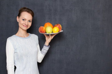 Portrait of happy young woman holding plate with ripe fresh fruits