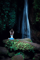 Woman sitting on the rock, practicing yoga. Young woman raising arms with namaste mudra near...
