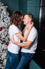 Loving married couple cuddling near Christmas tree, window