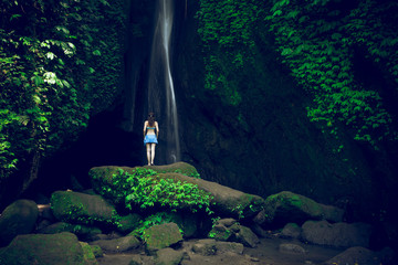 Young traveler woman at waterfall in tropical forest. View from back. Leke Leke waterfall, Bali. Slow shutter speed, motion photography.