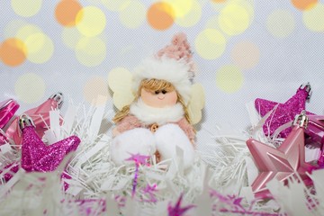 Plush fabric Christmas ornament little girl angel and star-shaped ornaments. Christmas still life.Stars baubles in purple tones and pink-white baby girl angel under the lights.