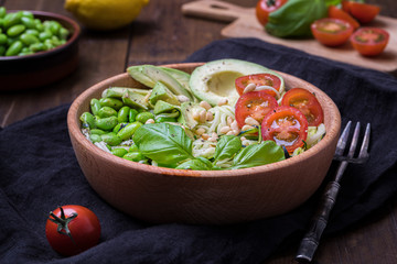 A fresh healthy salad with zoodles zucchini noodles, cherry tomatoes, avocado and edamame beans on a dark background
