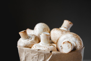 Mushrooms champignons in paper bag on a dark background. Close up. Place for text or advertising