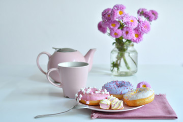 pink teapot, cup of tea and colorful delicious doughnuts