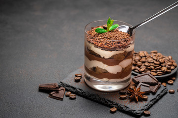 Classic tiramisu dessert in a glass cup and pieces of chocolate on stone cutting board on darl concrete background