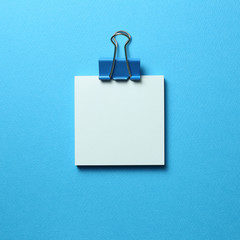 Blue memo pad sticky note and clip on blue background