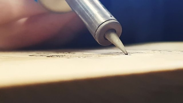 A soldering iron tip on the wood making smoke. An image burned in the wooden plot. Making an inscription by Burning Wood with a Soldering Iron. Writing text on the wood with a burning technique.