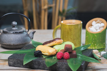 Sweet dessert, eclairs, raspberries and chocolate candies on a wooden table with decor in oriental, asian style.