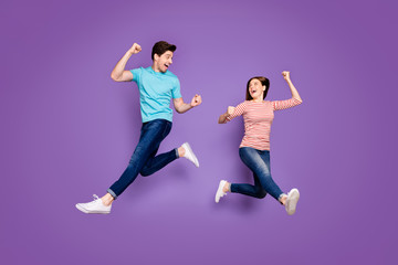 Fototapeta na wymiar Full body photo of funny two people guy lady jumping high rejoicing ecstatic achievement raise fists wear casual blue striped t-shirts jeans footwear isolated purple color background