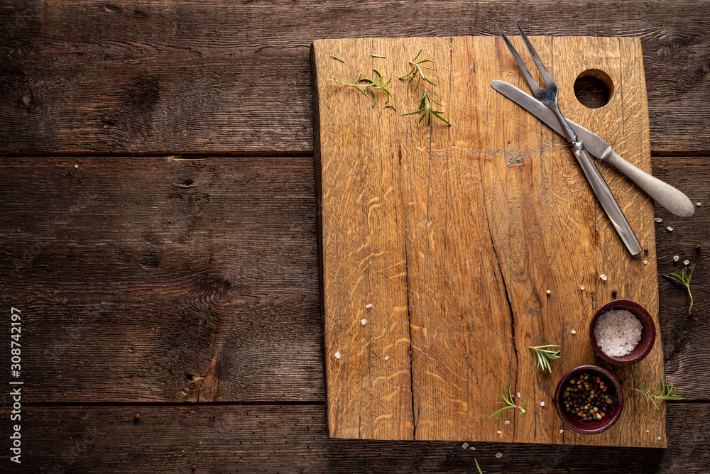 Wall mural Chopping board on dark, wooden table. Rosemary, pepper, salt. Copy space.