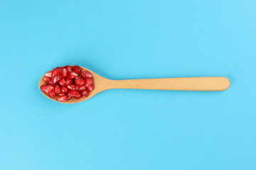 Red Pomegranate seed wooden spoon blue paper background