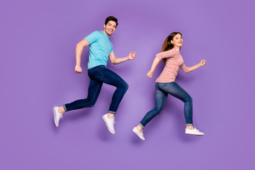 Fototapeta na wymiar Full body profile photo of crazy funky two people guy lady jumping high rushing season sales black friday wear casual blue striped t-shirts jeans shoes isolated purple color background
