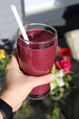 Pink / purple homemade berry and vegetable smoothie with vibrant color and plenty of vitamins. Healthy and delicious drink for sunny summer days. This is an outdoors closeup color photo with flowers.