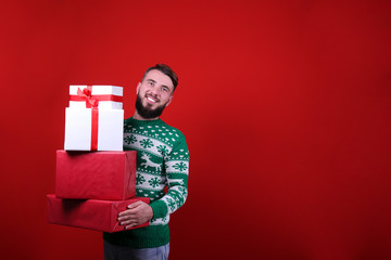 Studio portrait of handsome bearded man wearing christmas sweater with snowflake ornament, posing over the red wall, copy space for text. Festive background. Male with facial hair smiling.
