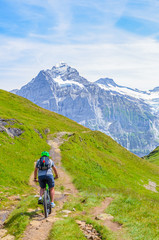Fototapeta na wymiar Mountain biker riding in amazing summer Alpine landscape. Snowcapped mountains in the background. Photographed on the trail from Grindelwald to Bachalpsee. Active vacation, people doing sport