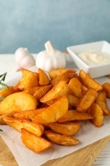 Slices of baked potato wedges, garlic, rosemary, white sauce on kitchen board against blue background, space for text. Closeup