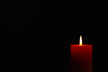 Glowing candle on black background, space for text
