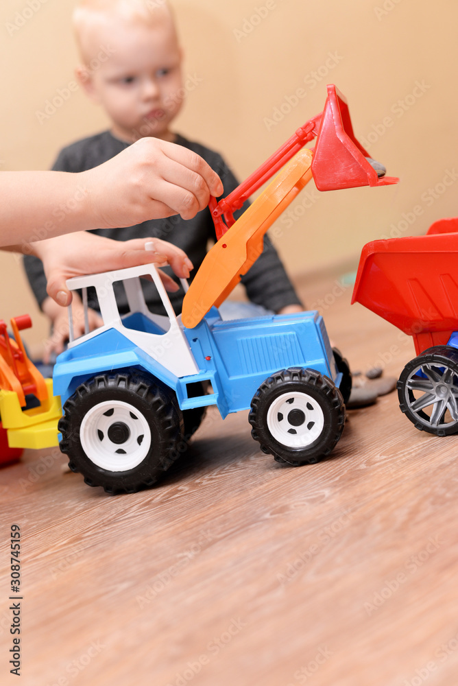 Wall mural Mom shows her son how to play with a toy tractor.