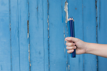 Hand Holding Blue Color Pencils against Blue Background