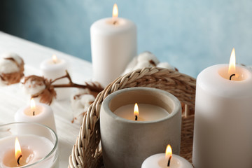Burning candles, basket and cotton on white wooden background, close up