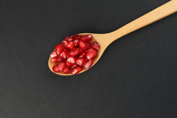 Red Pomegranate seed wooden spoon black paper background