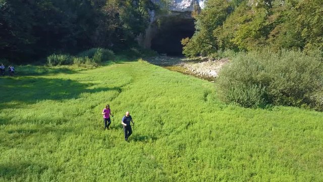 Couple hiking across green meadow near river Reka in Slovenian karst area