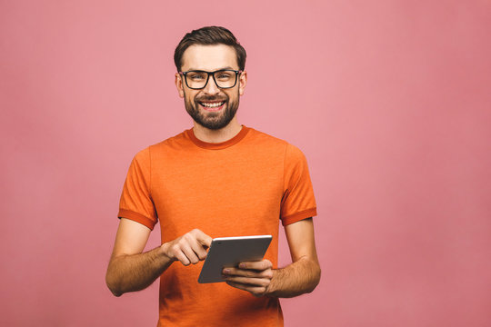 Happy Young Man In Casual Standing And Using Tablet Isolated Over Pink Background.