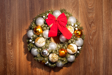 Christmas wreath with a red bow and Christmas toys balls made of beads on a wooden background of brown color.