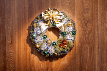 Christmas wreath with a golden bow and Christmas balls and balls of gray and blue color on a wooden background of brown color.
