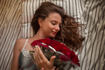 Good morning Attractive young woman in bed is holding bouquet of hundred red roses.