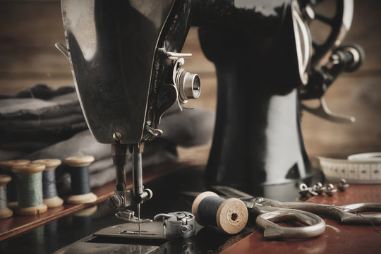 Old Antique Sewing Machine Close Up. Tailoring Scissors, Cloths And Wooden Spools Of Threads. Retro Tailor Workshop.