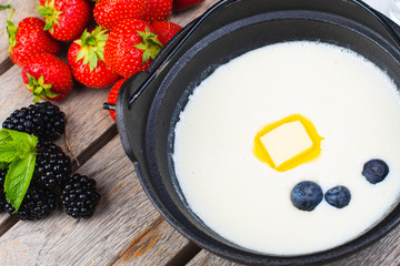 Traditional breakfast milk porridge with butter and berries on a wooden table.