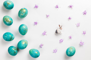 Fototapeta na wymiar Happy easter card. Stylish minimalistic composition of turquoise with gold easter eggs on a white background. Figurine of a rabbit and delicate spring flowers. Flat lay, top view, copy space