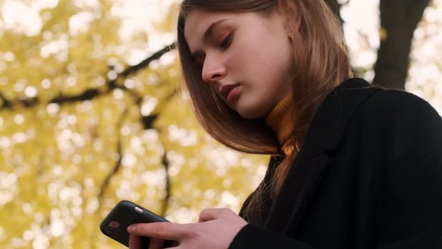 Portrait of confident girl in coat intently using cellphone walking alone outdoor