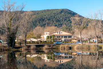 Fototapeta na wymiar Casa al otro lado del lago con reflejo, cielo azul y una montaña al fondo