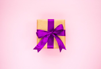 Giftbox tied with purple color ribbon on pink background. Flat lay style.