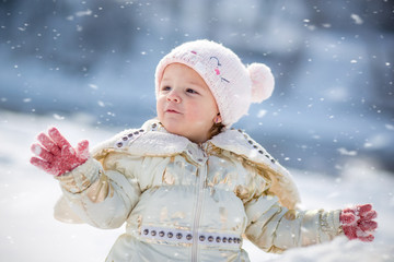 Little girl in white jacket having fun, playing outside, surrounded with snow.