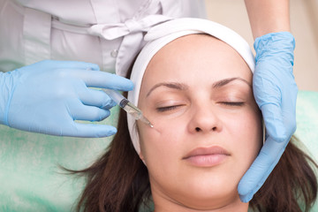 Fototapeta premium injection into the skin of the face of a young woman, close up. Doctor cosmetologist using a syringe with a needle, injects a remedy for facial wrinkles