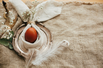 Stylish Easter brunch table setting with egg in easter bunny napkin. Modern natural dyed egg on napkin with bunny ears, flowers on vintage plate. Rustic Easter table decorations