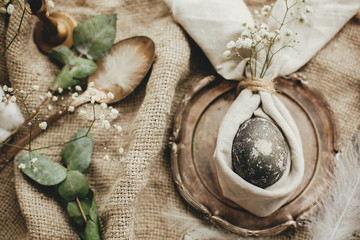 Stylish Easter brunch table setting with egg in easter bunny napkin. Modern natural dyed gray egg on napkin with bunny ears, flowers on vintage plate. Rustic Easter table decorations