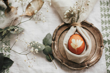Rustic Easter table decorations. Modern natural dyed egg on napkin with bunny ears, flowers on vintage plate.Stylish Easter brunch table setting with egg in easter bunny napkin.