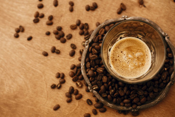 Hot espresso with foam in glass cup on vintage plate with aromatic roasted coffee beans on wooden table. Flat lay with copy space. Alternative Coffee brewing concept.